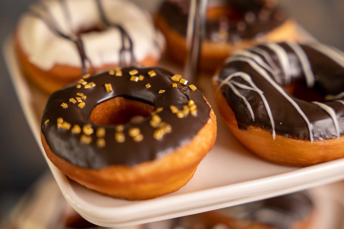 Chocolate glazed donut with gold sprinkles on a cake stand, more glazed donuts behind