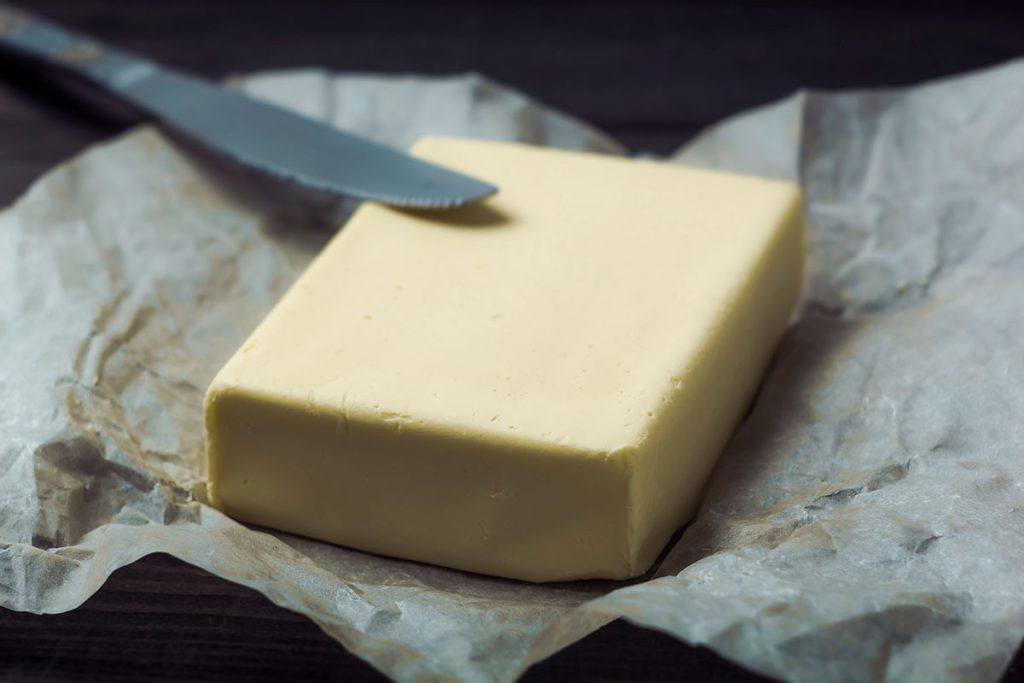 A block of unsalted butter on a piece of parchment paper with a butter knife resting beside it. The butter appears smooth and creamy, ready for use in baking or cooking.