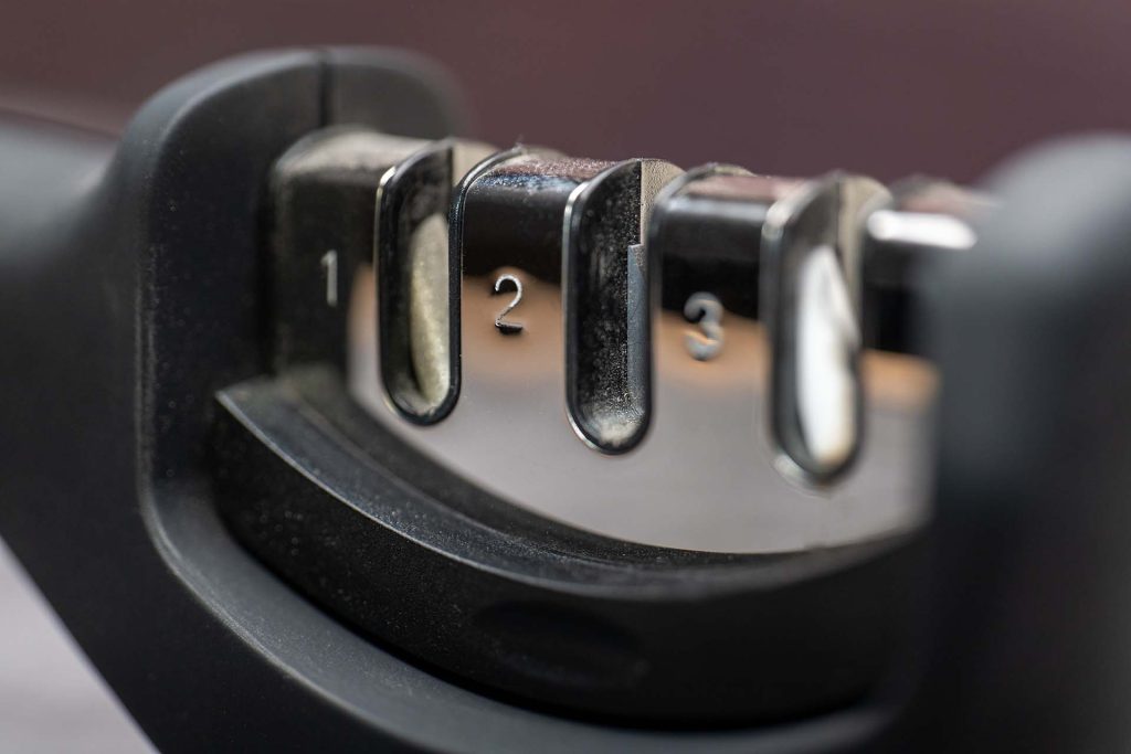 A detailed close-up image of the three numbered sharpening slots (1, 2, and 3) on a black handheld knife sharpener, showing the different stages of the sharpening process. The image emphasizes the tool's functionality and precision in sharpening kitchen knives.