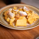Austrian Kaiserschmarrn dusted with powdered sugar on a plate set on a wooden board
