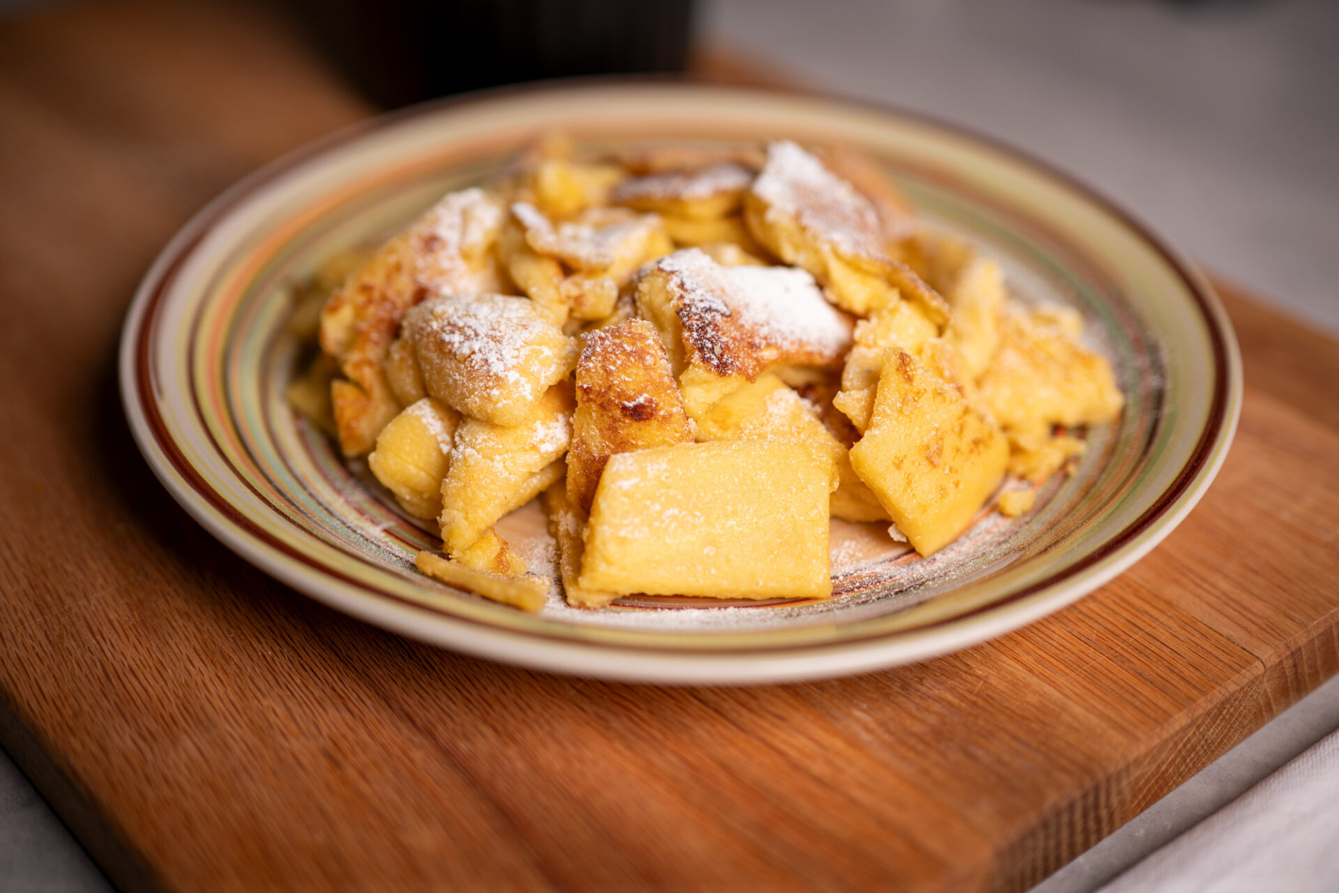 Austrian Kaiserschmarrn dusted with powdered sugar on a plate set on a wooden board
