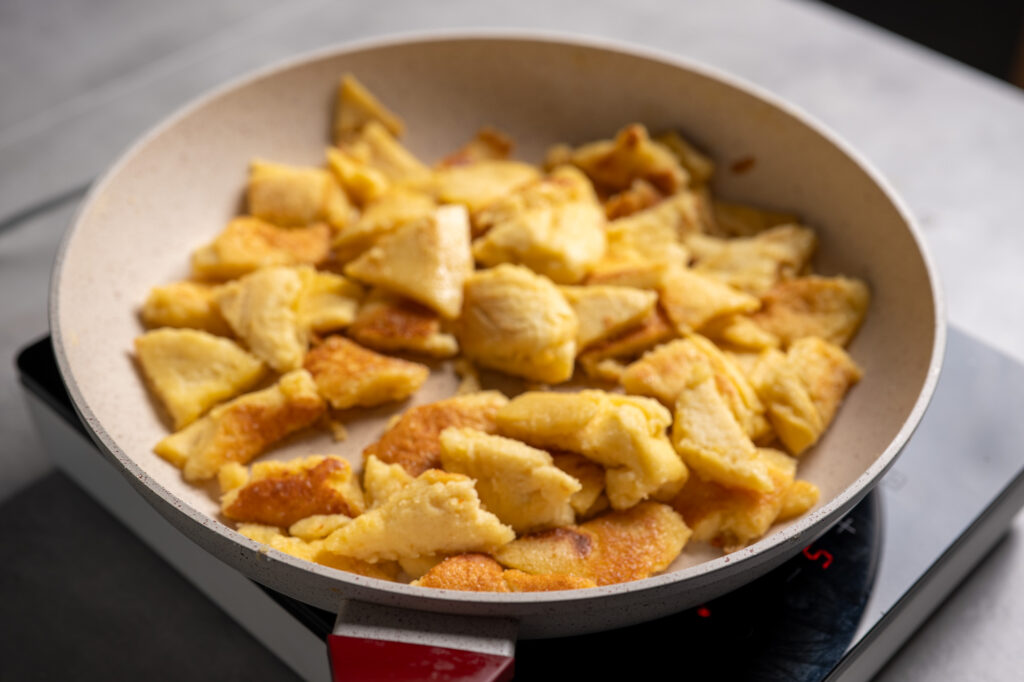 Torn Kaiserschmarrn pieces caramelising in a frying pan