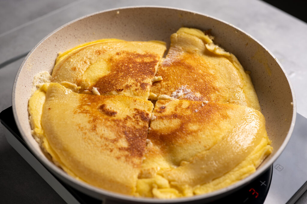 Kaiserschmarrn quarters flipped in the pan showing a golden brown crust