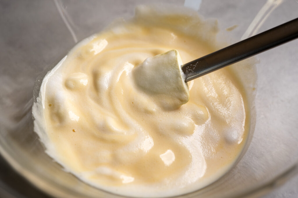 Whipped egg whites being folded into Kaiserschmarrn batter with pale streaks still visible