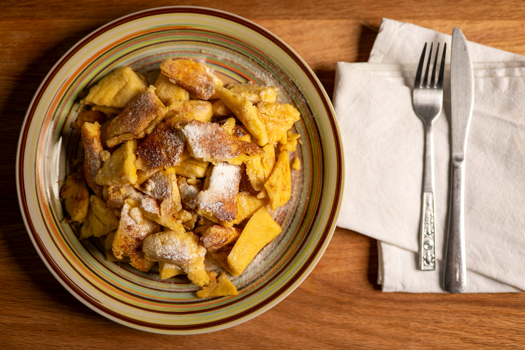 Overhead view of Kaiserschmarrn served on a striped plate with fork and knife on a linen napkin