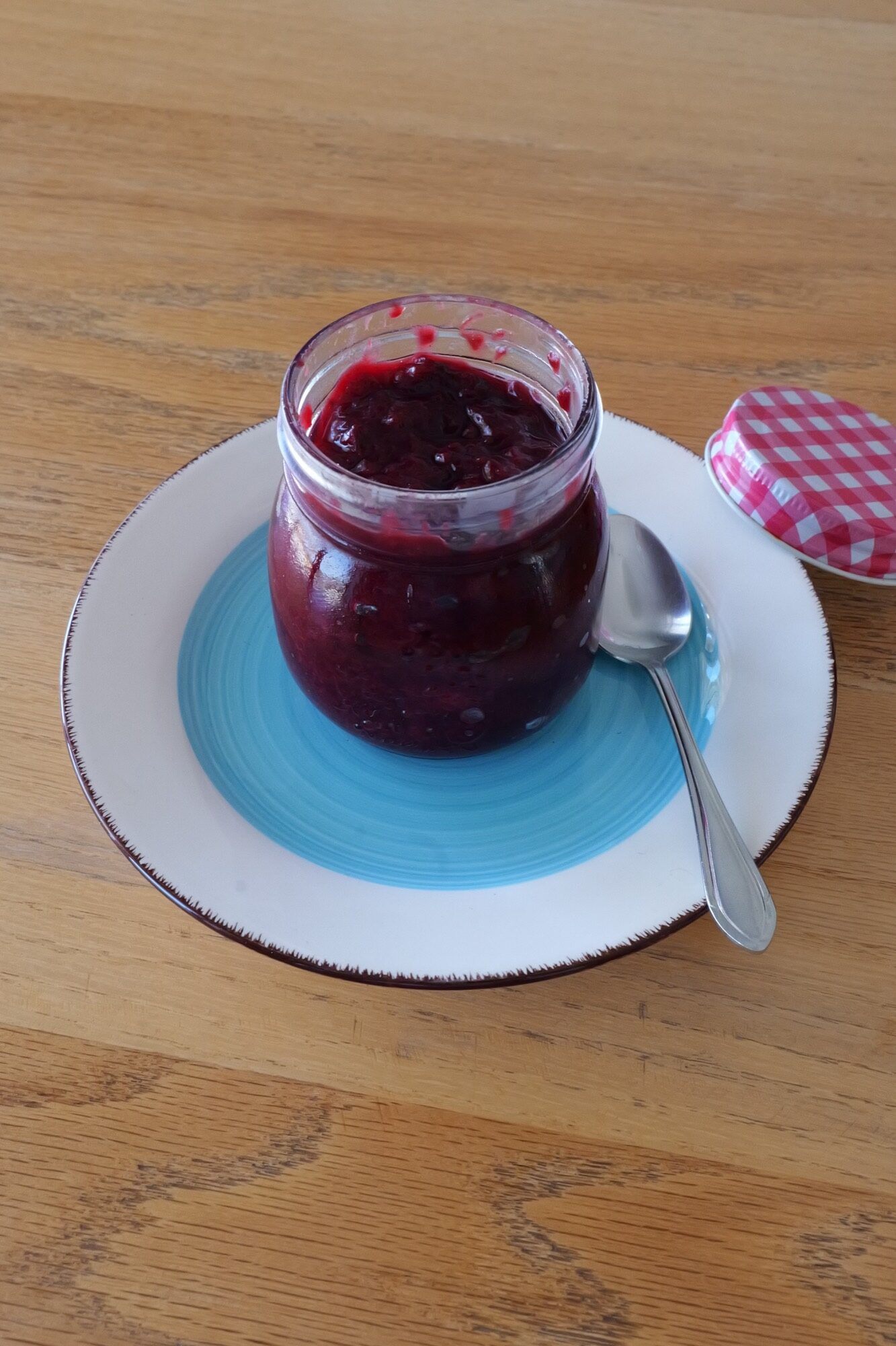 Open jar of dark homemade Powidl with a spoon resting beside it