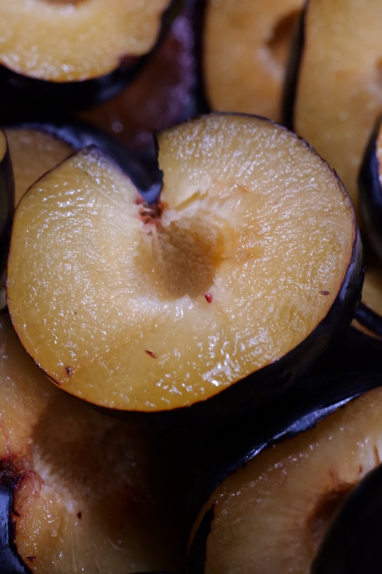 Glossy halved ripe plums ready for slow reduction